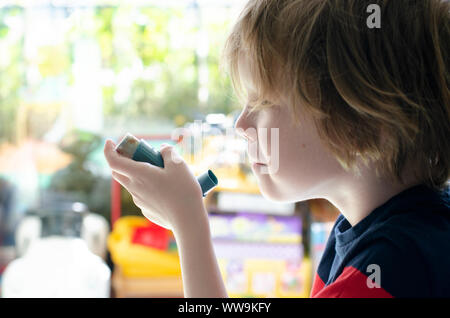 Vereinigtes Königreich, 10. Juli 2019: kleiner Junge vor einem Fenster mit einem Ventolin inhaler Stockfoto