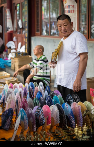 Xian, China - Juli 2019: Ältere Menschen verkaufen bunte Papier Ventilatoren an einem heißen Tag auf der Straße im muslimischen Viertel Stockfoto