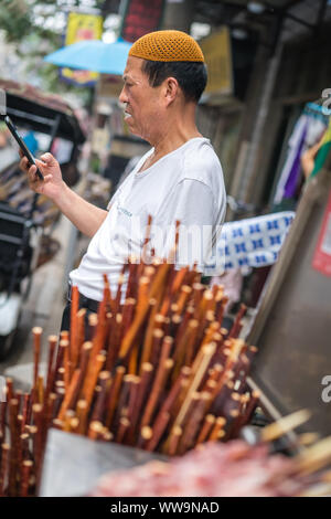 Xian, China - Juli 2019: Gelangweilt essen Verkäufer sein Smartphone Kontrolle auf einem im muslimischen Viertel stall in Xian, Provinz Shaanxi Stockfoto