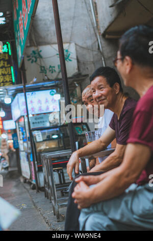 Xian, China - Juli 2019: Gruppe von männlichen Freunden reden und Chatten hinter einem Markt im muslimischen Viertel in Xian, Provinz Shaanxi Stadt Abschaltdruck Stockfoto