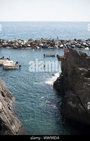 Manarola, Italien - Juli 2, 2018: An einem heißen Sommer Tag, badegäste Sprung vom Felsen ins Meer in Manarola, einer der fünf traditionellen Cinque Terre fi Stockfoto