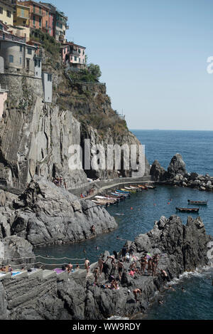 Manarola, Italien - Juli 2, 2018: An einem heißen Sommer Tag, Badegäste sammeln entlang der felsigen Küste ins Meer in Manarola, einer der fünf tradit zu springen Stockfoto