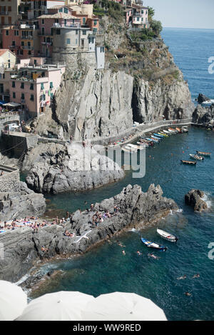 Manarola, Italien - Juli 2, 2018: An einem heißen Sommer Tag, Badegäste sammeln entlang der felsigen Meer in Manarola, einer der fünf traditionellen Cinque Terre Fisch Stockfoto