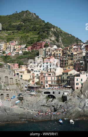 Manarola, Italien - Juli 2, 2018: Die bunten Häuser des Manarola Fischerdorf Aufstieg Aufstieg über Meer Badenden an einem heißen Sommer Tag, in Cinque T Stockfoto