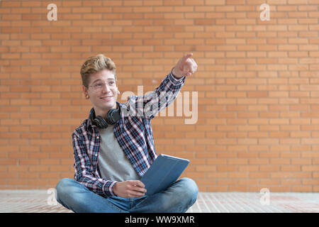 Ausdrucksstarkes Gesicht eines Jungen, der an einem bestimmten Punkt sieht und deutet mit einer Hand festhalten und mit der anderen Hand hält eine Tablette. Stockfoto