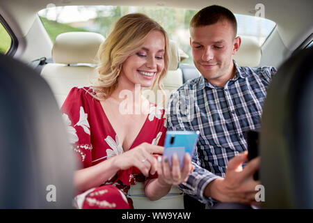 Foto der glücklichen Frauen und Männer mit dem Telefon in der Hand in den Rücksitz des Autos während der Sitzung Stockfoto