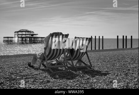 Ein Paar, das sich im Spätsommer an der Südküste Englands auf den Liegestühlen am Brighton Beach entspannt Stockfoto