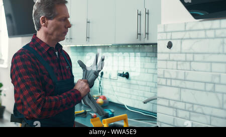 Porträt von Ernst kaukasischen repairmanin einheitliche stehen in der Küche. Er trägt Handschuhe in Orer zu arbeiten beginnen. Reparatur Service Konzept. Horizontale Schuß Stockfoto