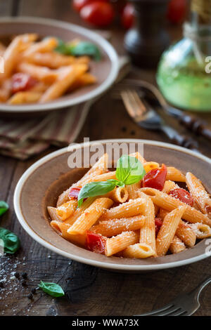 Teller Pasta Penne mit Cherry Tomaten, frischem Basilikum und Parmesan - Pasta al Pomodoro. Im rustikalen Platten für ein Abendessen für Zwei serviert. Stockfoto