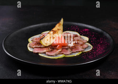 Kantige Stücke mit karamellisierten Birnen auf einem schwarzen Keramik Teller. Gebackenes Fleisch in dünne Stücke geschnitten Stockfoto