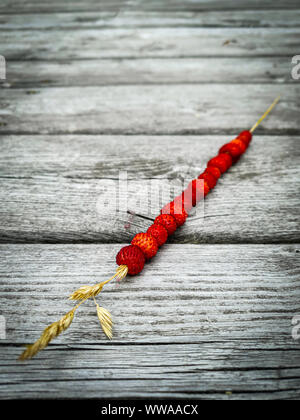 Wilde Erdbeeren auf einem Strohhalm. Sommer Konzept. Rustikalen Holztisch im Hintergrund. Stockfoto