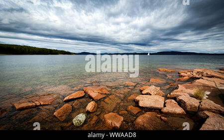 Einsam Segel Boot im Archipel. Dramatische Himmel über steinigen Strand Küste und seichtem Wasser. Storsand, Hohe Küste im Norden Schwedens. Stockfoto