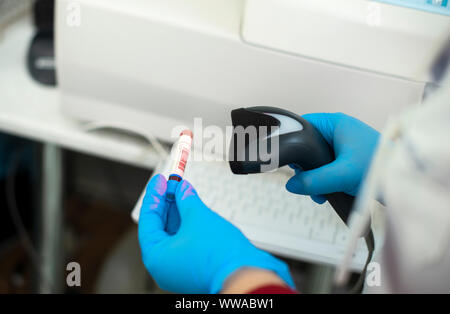 Barcodescanner und Reagenzglas über Monitor von kompletten Blutbild Analyzer im Hintergrund. Stockfoto