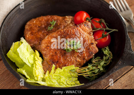 Parmesan verkrusteten Schweinekoteletts in Schwarz mit Cherry Tomaten und Salat Salat Pfanne serviert Stockfoto