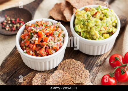 Traditionelle lateinamerikanische mexikanische Soße Guacamole und Salsa mit glutenfreien Chips auf Holz Schneidebrett Stockfoto