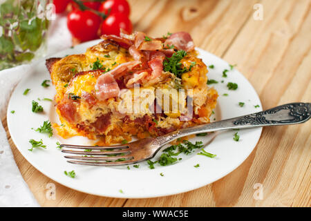 Cheesy Gratin mit süssen Kartoffeln, Speck, Rosenkohl, Eier und Tomaten auf hellem Holztisch Stockfoto