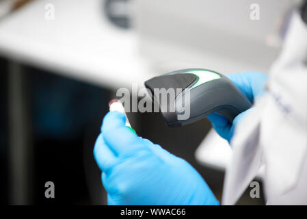 Barcodescanner und Reagenzglas über Monitor von kompletten Blutbild Analyzer im Hintergrund. Stockfoto