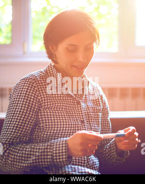 Schließlich schwanger. Attraktive junge Frauen bei Schwangerschaft Test suchen und lächelnd, während sie auf dem Sofa zu Hause sitzen Stockfoto