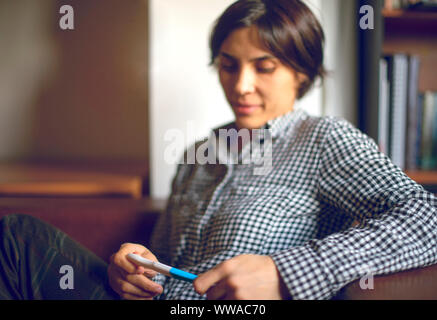 Schließlich schwanger. Attraktive junge Frauen bei Schwangerschaft Test suchen und lächelnd, während sie auf dem Sofa zu Hause sitzen Stockfoto