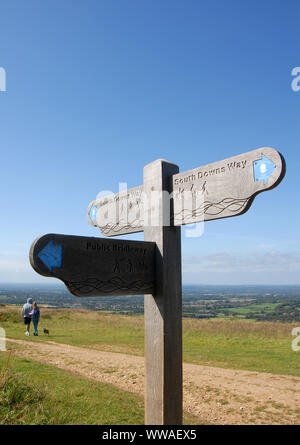 South Downs, Sussex, England, UK. Ein Mann und eine Frau mit einem Hund spazieren auf dem South Downs Way in Sussex. Ein Wegweiser zeigt die Route der South Downs Way. Stockfoto