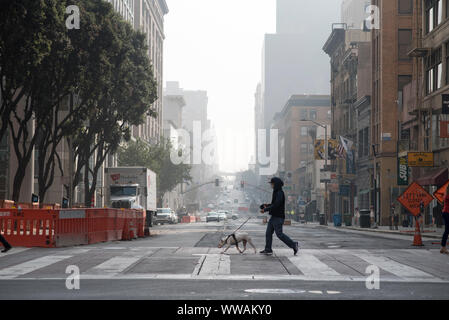 San Francisco, Kalifornien - 17. November 2018: Ein Mann mit einem Luft Filterung Maske geht seinen Hund über 2. Straße. Stockfoto