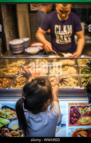 Xian, China - Juli 2019: Kleines Mädchen kaufen Essen vom Markt Anbieter auf der Straße im muslimischen Viertel Stockfoto