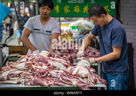 Xian, China - Juli 2019: Zwei Männer Arbeiter schneiden und die Trennung von Lamm und Rind Karkasse Fleisch und Knochen, die Street Food Anbietern im muslimischen Viertel Stockfoto