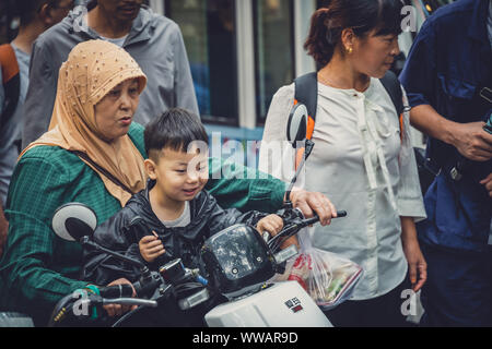 Xian, China - Juli 2019: muslimische Frau mit ihrem Sohn sitzen auf einem Roller auf der Straße im muslimischen Viertel Stockfoto