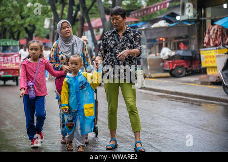 Xian, China - Juli 2019: Muslimische Familie einkaufen und wandern im Regen auf der Straße im muslimischen Viertel Stockfoto