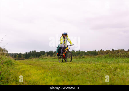 Männliche Radfahrer Reisenden mit einem Rucksack und ein Sattel Tasche Fahrten durch einen Herbst Wiese an einem bewölkten Tag Stockfoto