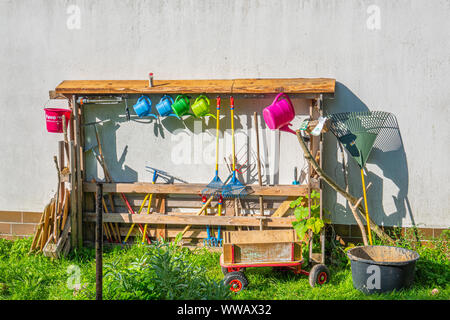 Auf einer weißen Hauswand in einem Kindergarten steht ein Regal mit verschiedenen Garten Werkzeuge gefüllt für Kinder Stockfoto