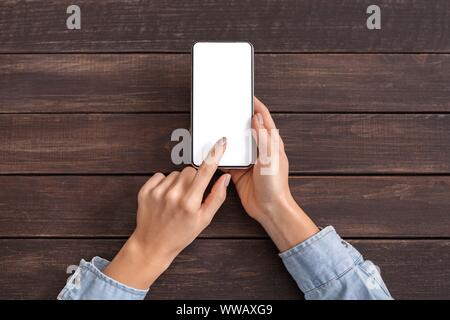 Weibliche Hände berühren Smartphone mit leeren Bildschirm auf Holz- Hintergrund Stockfoto