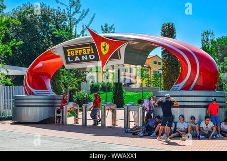 Eine Gruppe von Menschen sitzt auf dem Bürgersteig vor dem Eingang des Ferrari Themenpark Port Aventura Stockfoto