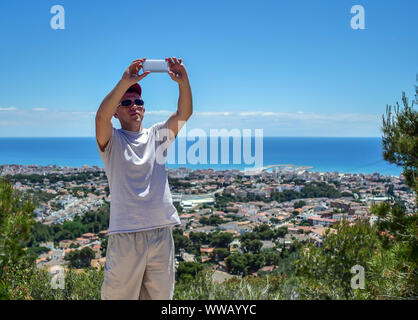 Junger Mann nimmt einen selfie auf dem Hintergrund einer Regelung durch das Meer Stockfoto