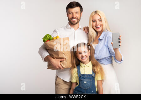 Familie mit leeren Handy Bildschirm Holding Grocery Bag, Studio Shot Stockfoto