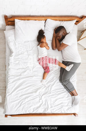 Kleines afrikanisches Mädchen schlafen mit Papa auf große Eltern ohne Zustellbett. Stockfoto