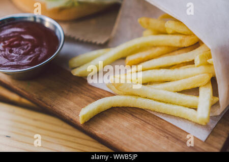 Frische leckere Burger und Pommes frites auf Holztisch. Pommes frites und BBQ Soße auf Holzplatte. Street Food Burger und Bratkartoffeln. Ungesunde Nahrung Stockfoto