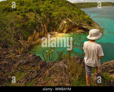 Ein kleiner Junge in einen weißen Hut blickt auf Little Bay, Anguilla, BWI. Unzugänglich ausser mit dem Boot oder mit dem Seil. Stockfoto