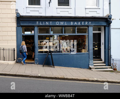 Eine Person, die in die Flint Owl Bakery in der Neiged High Street, Lewes, geht, während sie durch das Fenster sieht, wie der Barista Kaffee vom Kunden nimmt. Stockfoto