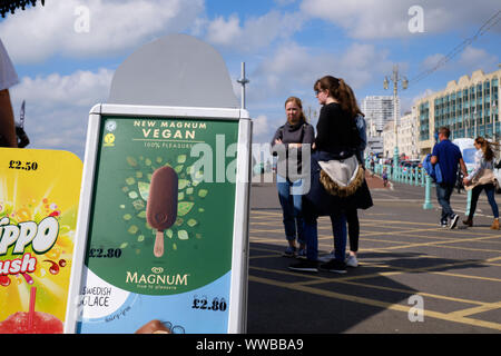 Vegan Magnum Werbung Anzeige auf dem Brighton Ufer entlang. Mit jungen Damen warten, von Kiosk zu bestellen, an einem kühlen Herbst sonniger Tag Stockfoto