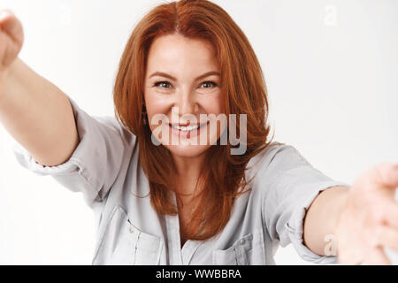 Freudige erfolgreiche stilvolle Rothaarige schöne Frau mittleren Alters, die selfie halten Sie die Kamera mit beiden Händen toothy Lächeln erfreut, perfekte Aufnahme Stolz nehmen Stockfoto