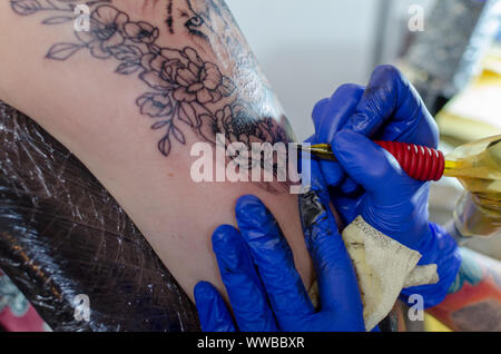 WROCLAW, Polen - 11. August 2019: Tattoo Wettbewerb. Prozess der Herstellung floral Tattoo auf eine Frau Oberarm. Close-up, selektiver Fokus Stockfoto