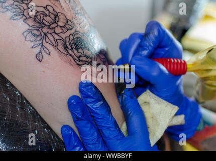 WROCLAW, Polen - 11. August 2019: Tattoo Wettbewerb. Prozess der Herstellung floral Tattoo auf eine Frau Oberarm. Close-up, selektiver Fokus Stockfoto