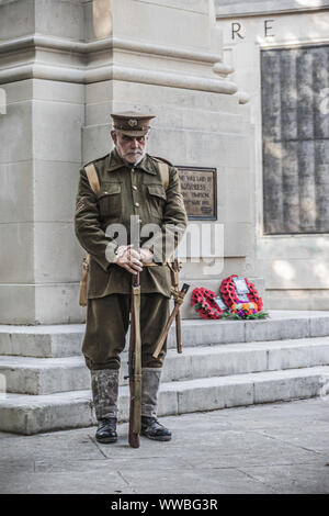 Ein Mann im Ersten Weltkrieg Soldaten Uniform neben einem britischen Kriegerdenkmal mit roter Mohn Kränze auf stehend Stockfoto