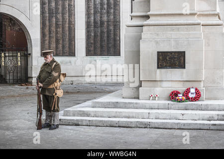 Ein Mann im Ersten Weltkrieg Soldaten Uniform neben einem britischen Kriegerdenkmal mit roter Mohn Kränze auf stehend Stockfoto