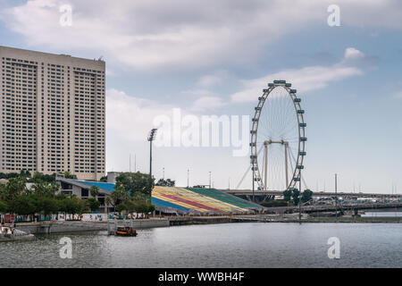 Singapur - 20. März 2019: Der Schwimmer ist eine Stufe über dem Wasser der Marina mit Schrägen bunte Bereich für Zuschauer. Der Flyer ist ein hohes Riesenrad. Stockfoto
