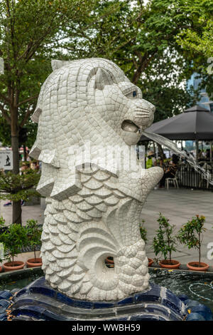 Singapur - März 20, 2019: Nahaufnahme von kleinen weissen Merlion Statue und Brunnen unter dem grünen Laub am Fuß des großen Bruders, Stockfoto