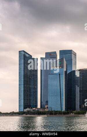 Singapur - März 20, 2019: Porträt der Wolkenkratzer des Financial District auf der Seite der Bucht und das Meer unter schweren cloudscape. Wasser von Marina vor. Stockfoto