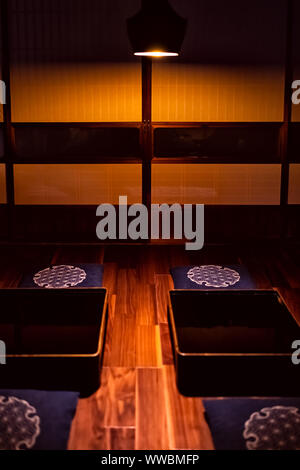 Traditionelle Japanische machiya Haus Ryokan mit Schwarz lackiertem Holz Tisch, Kissen Kissen, beleuchtete Lampe Licht und schieben Papier Türen an dunklen n Stockfoto