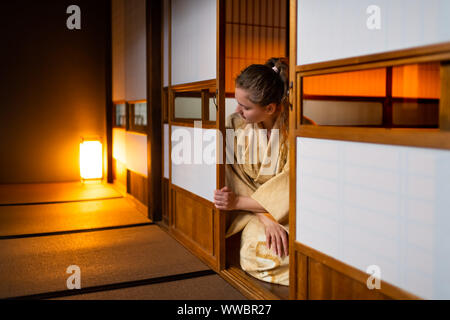 Die traditionellen japanischen Ryokan Zimmer mit Gaijin kaukasische Frau im Kimono, Tabi Socken Eröffnung shoji Schiebetüren Papier Türen sitzen auf Tatami Matten Boden Stockfoto